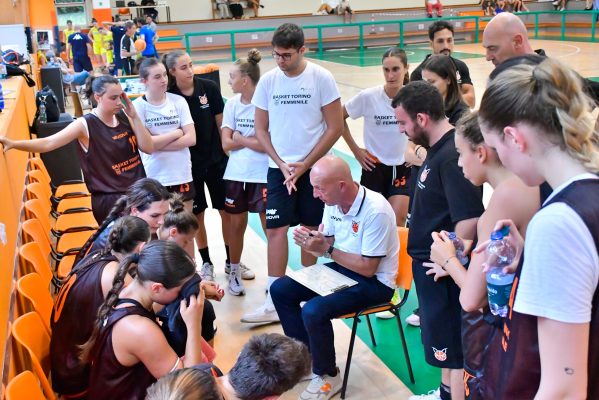 Timeout del Basket Torino Femminile durante una partita La squadra del Basket Torino Femminile riunita durante un timeout, con l'allenatore che fornisce indicazioni tattiche. Le giocatrici ascoltano attentamente mentre si preparano per il proseguimento della partita. Lo sfondo mostra il campo e l'ambiente di gioco.